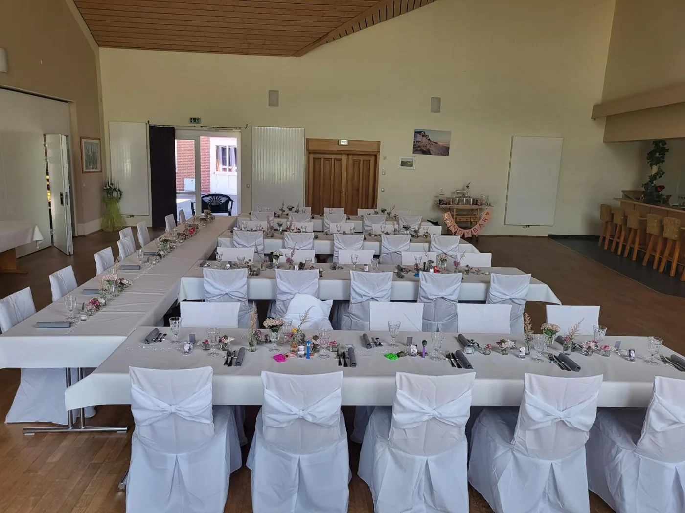 Festlich eingedeckter Saal mit runden Tischen und heller Holzdecke.