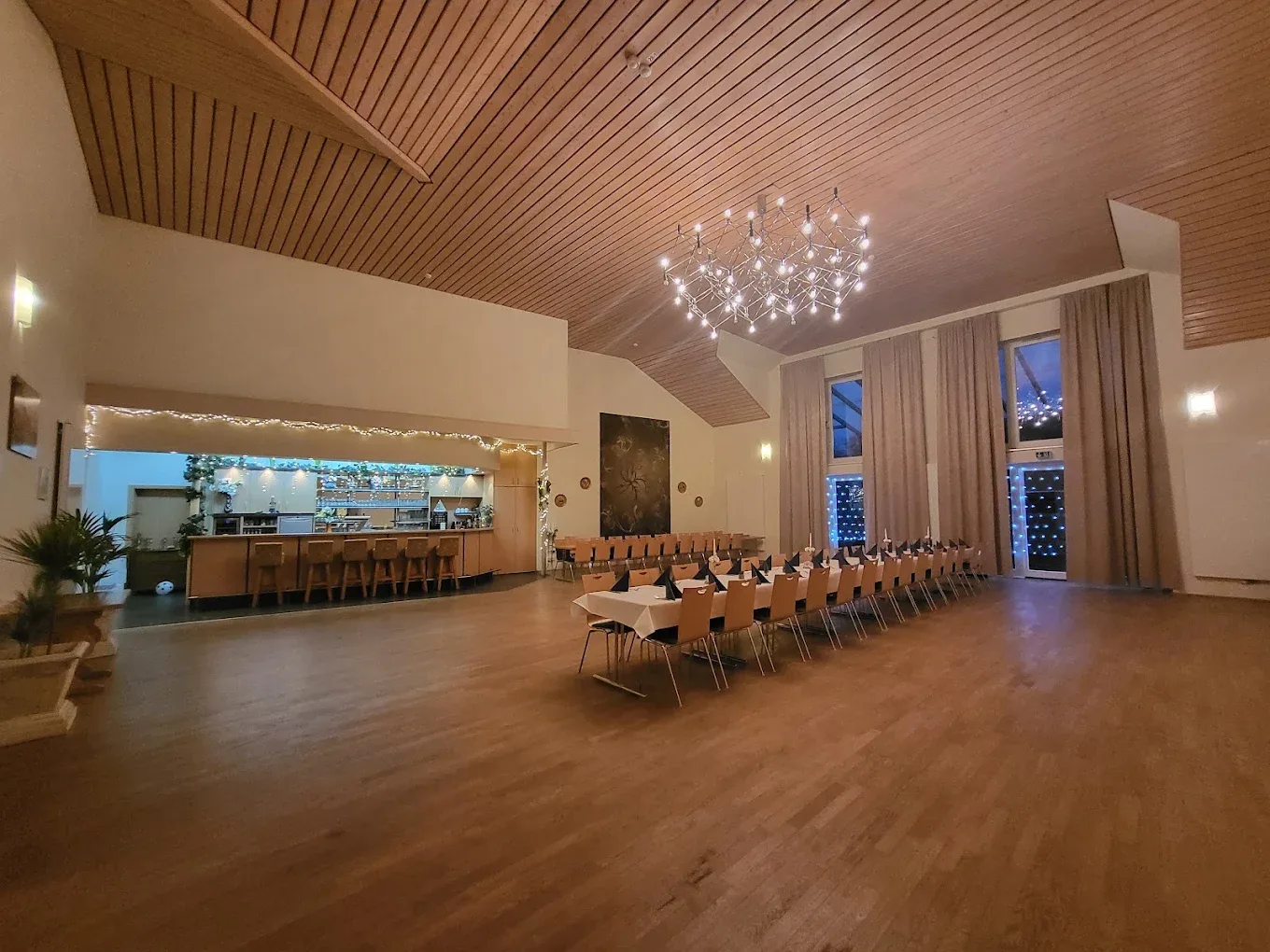 Festlich beleuchteter Saal am Abend: Sternleuchter, warmes Holz, Bar und Lichterketten — bereit für eine georgische Tafel